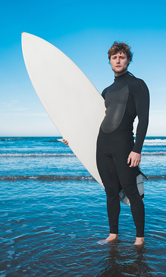 surfer wearing a full wetsuit and carrying a surfboard